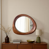 Round wooden mirror on a wall with a lamp and books on a wooden console table.