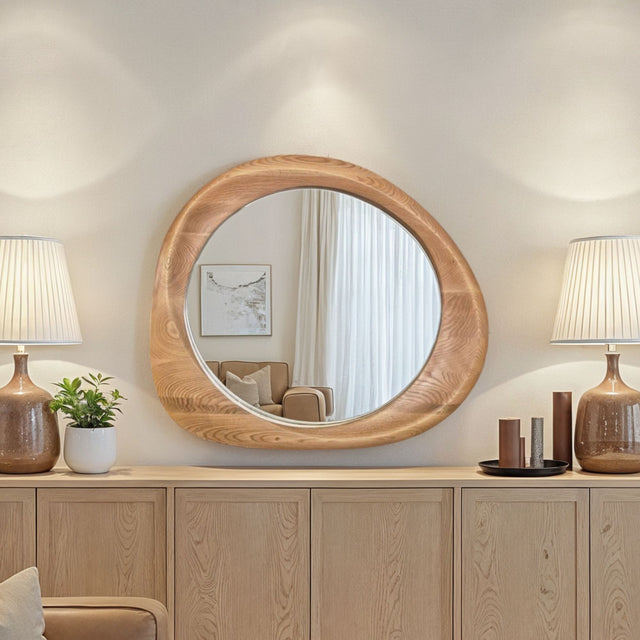 Round wooden mirror on a wooden cabinet with lamps and decor items.