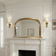 Gold-framed mirror above a fireplace with wall sconces on either side.