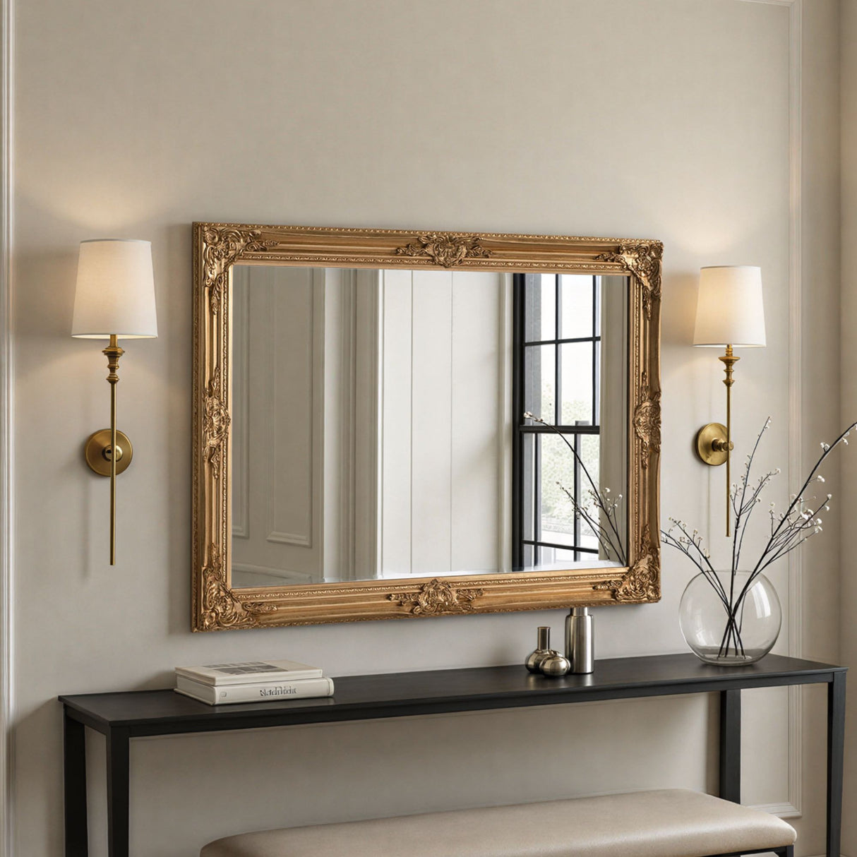 Decorative gold-framed mirror above a console table with wall lights and a vase.