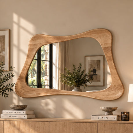 An organic-shaped wooden wall mirror with a thick, wavy oak-look frame, mounted on a beige wall above a wooden console table in a styled interior setting.