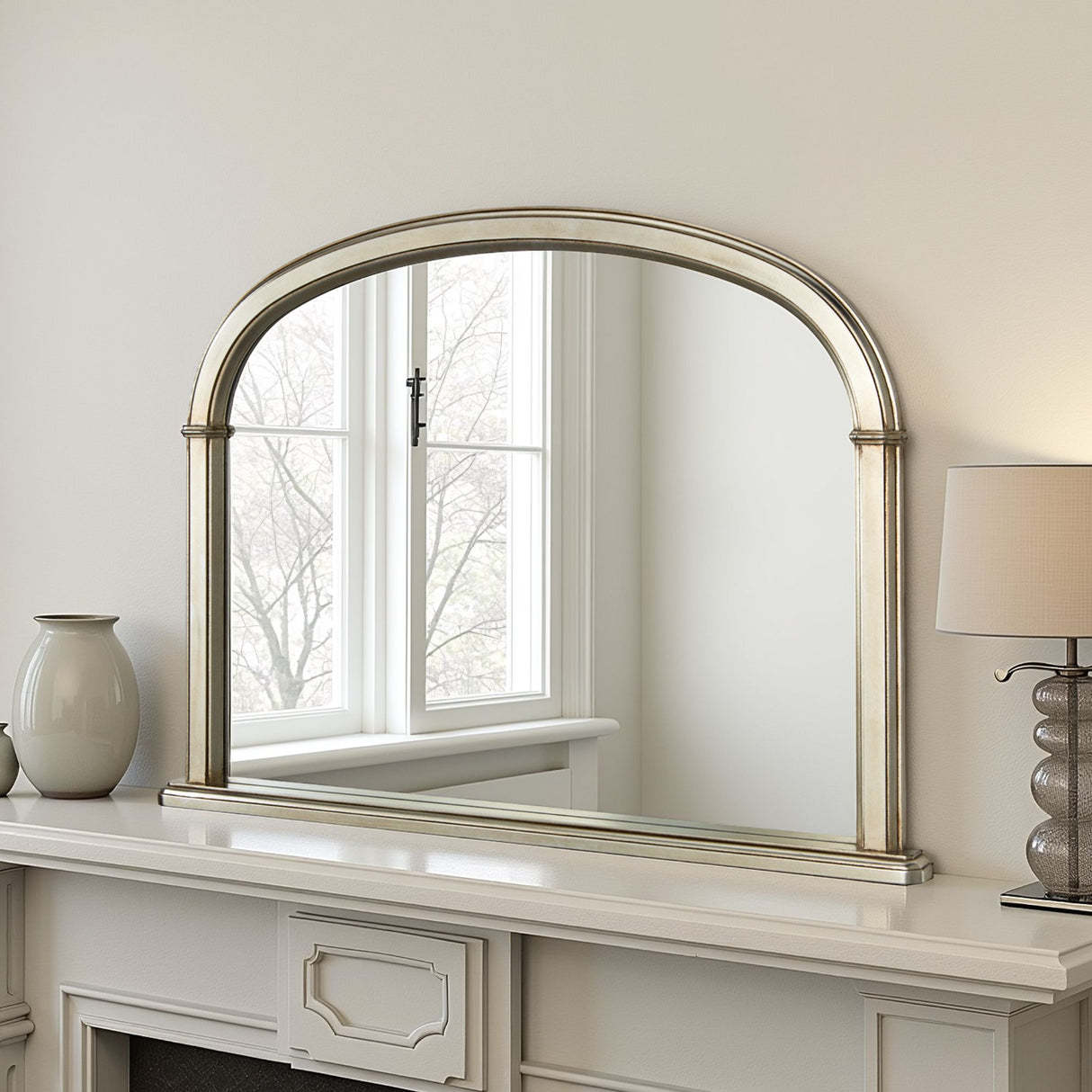 Decorative mirror with silver frame on a white wall above a fireplace.