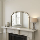 Decorative mirror above a fireplace with a lamp and vases on the mantel.