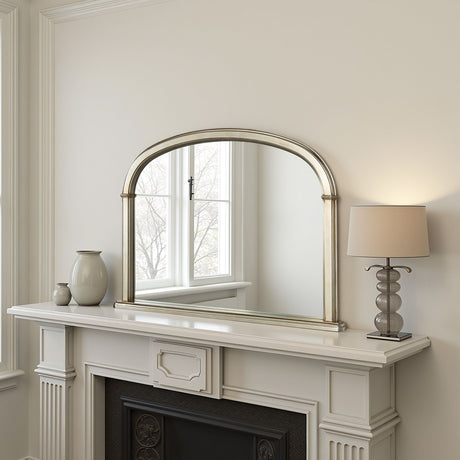 Decorative mirror above a fireplace with a lamp and vases on the mantel.