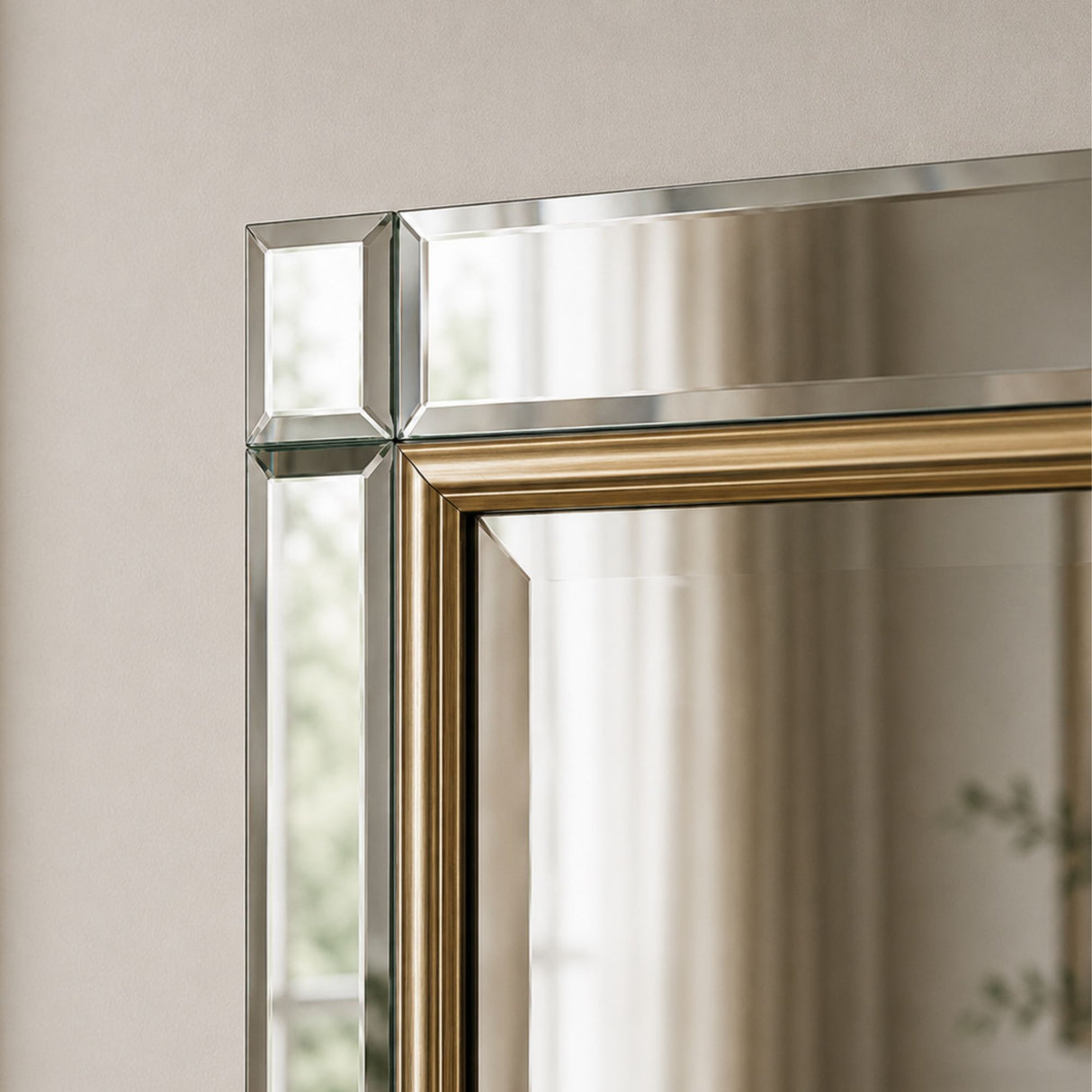 Close-up of a rectangular wall mirror with a polished silver-toned frame and a gold inner border, reflecting a softly lit interior.