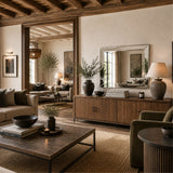 A styled living room interior with a wooden credenza, matching wood coffee table, lamps, upholstered chairs, woven rug, and large mirror reflecting the room. No person or animal is present, but this is still a real interior environment rather than a clean isolated product shot, so subject_type is Lifestyle.